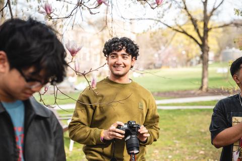 A student holds a camera and smiles